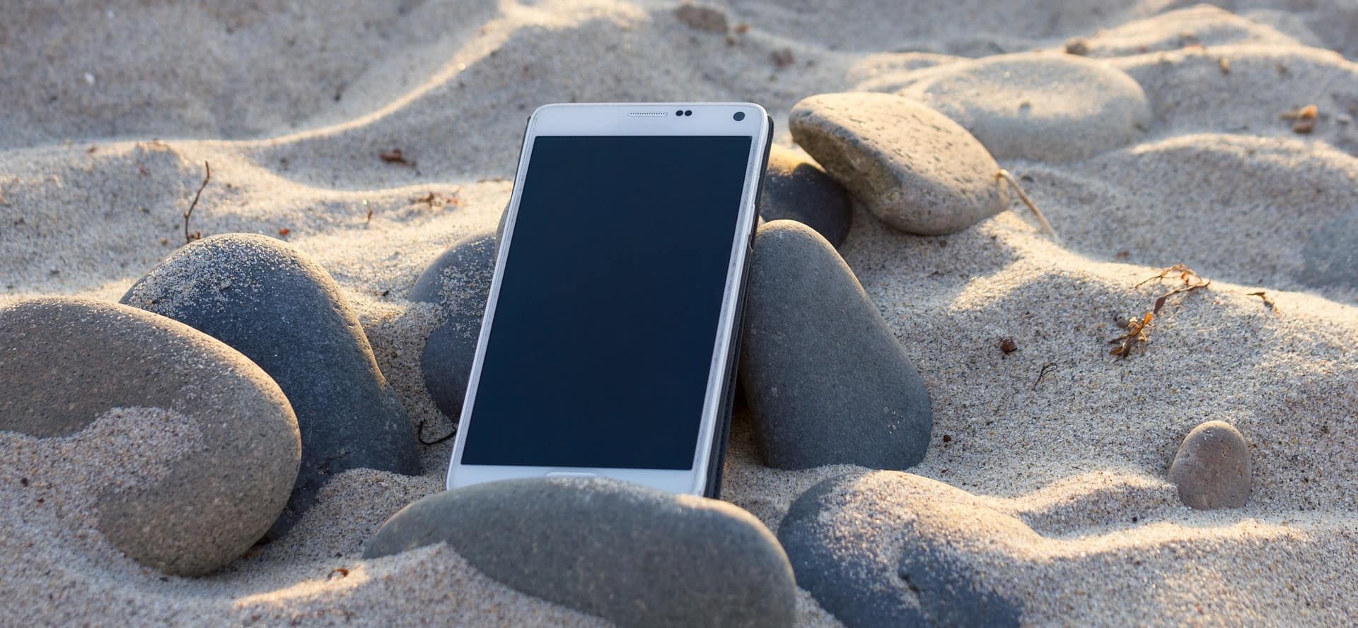 Téléphone sur la plage illustrant un service à l’écoute, réactif, accessible et un engagement permanent pour vous accompagner dans vos besoins.